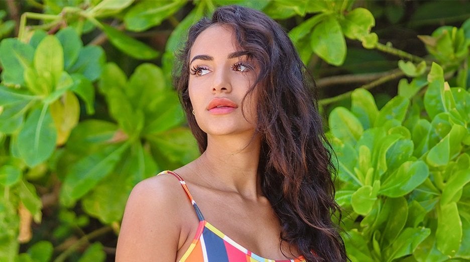 Woman with beautiful, nourished, non-frizzy hair wearing a colorful top against an exotic leafy background.