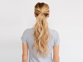 A woman with long blonde hair is seen from behind, showcasing a wavy, low ponytail.