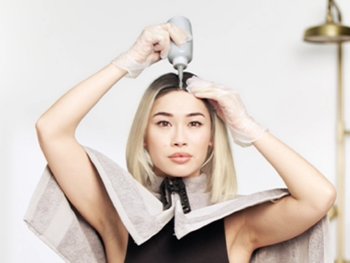 Asian-Pacific model applying hair dye to the brown roots of her otherwise, platinum blonde short hair.