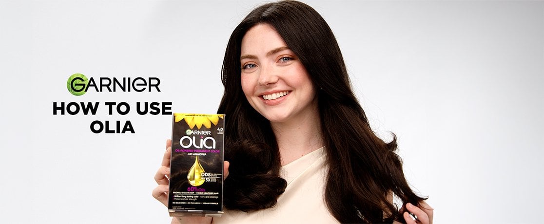 Smiling woman with long dark hair holds an oil-powered permanent hair color box in a "How to Use" tutorial graphic.