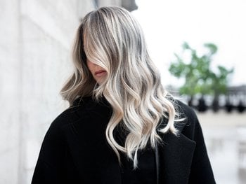 A person with shoulder-length, ash-blonde/silver hair, illustrating cool or ash shades to neutralize warm tones.
