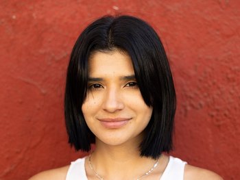 A woman with fair skin and natural black hair looks directly at the camera.