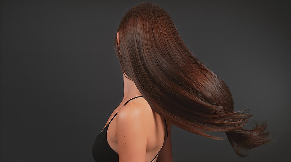 Beautiful seductive brunette woman on dark background shiny brown healthy hair waving on wind