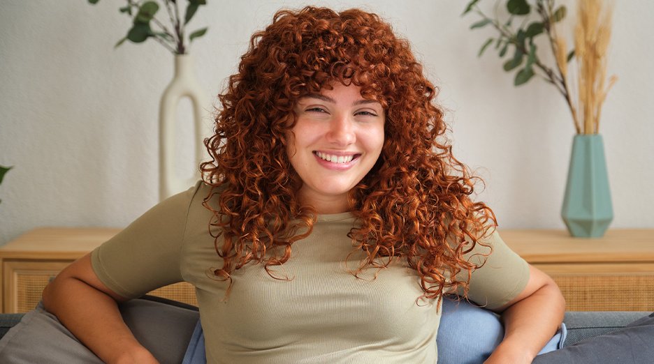 Woman smiling with curly, copper colored hair.