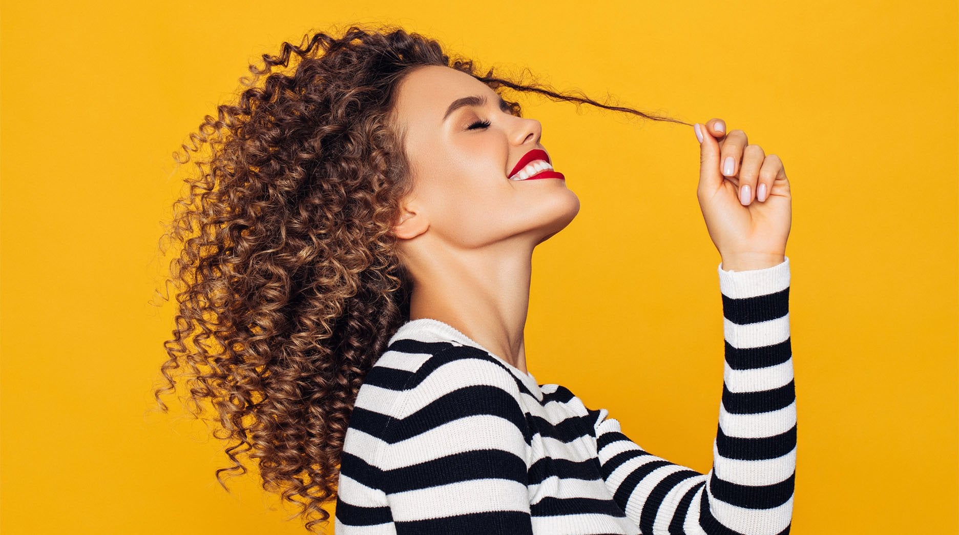 Side profile of model with curly curl stretching one curl as she slightly tilts head back and smiles.