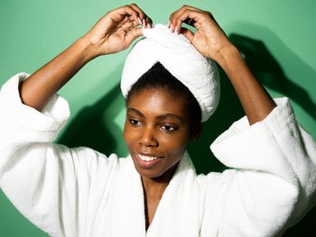 A woman with a white towel turban on her head smiles, demonstrating how to protect curls while drying.