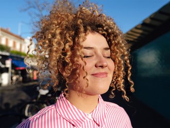 A close-up of a person with curly hair, eyes closed, enjoying the feel of air-dried curls.
