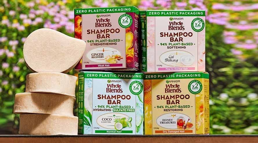 Garnier Whole Blends Shampoo Bars in zero plastic packaging, featuring four varieties: Strengthening (Ginger Recovery), Softening (Oat Delicacy), Hydrating Sulfate-Free (Coco & Aloe Vera), and Restoring (Honey Treasures). The image shows the 94% plant-based shampoo bars, both boxed and unboxed, highlighting their sustainable and diverse hair care benefits.