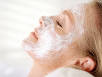 A person reclines with a white face mask applied.