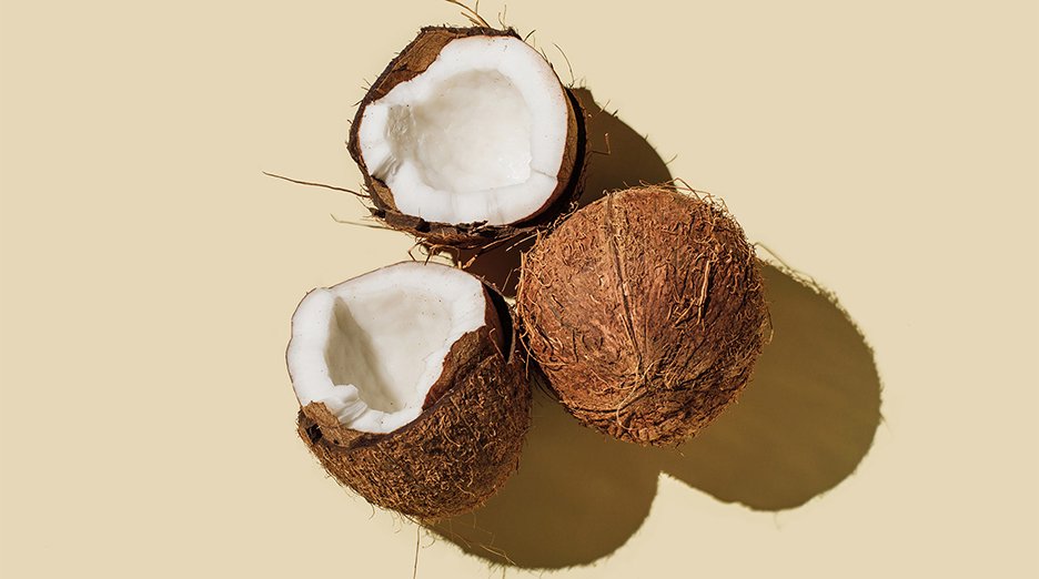Three halves of a coconut are positioned against a light tan background.