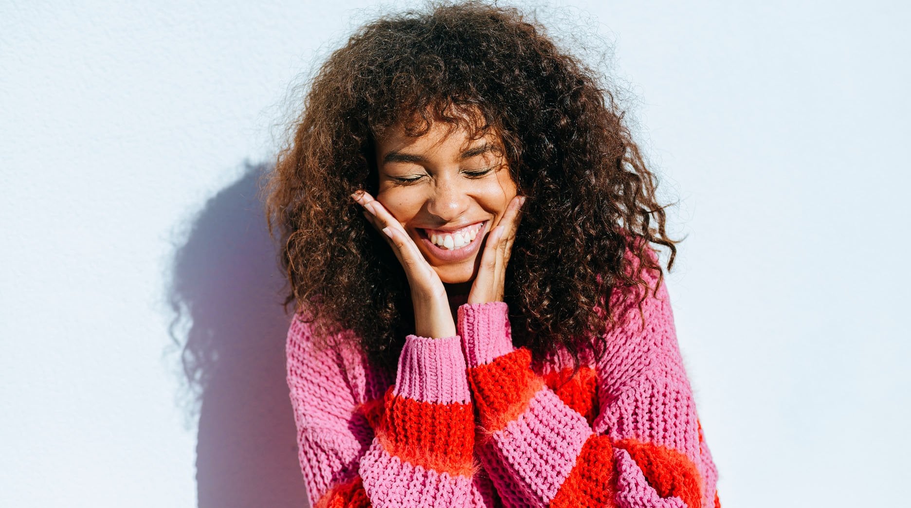 Woman with long and curly hair smiling with hands close to her face