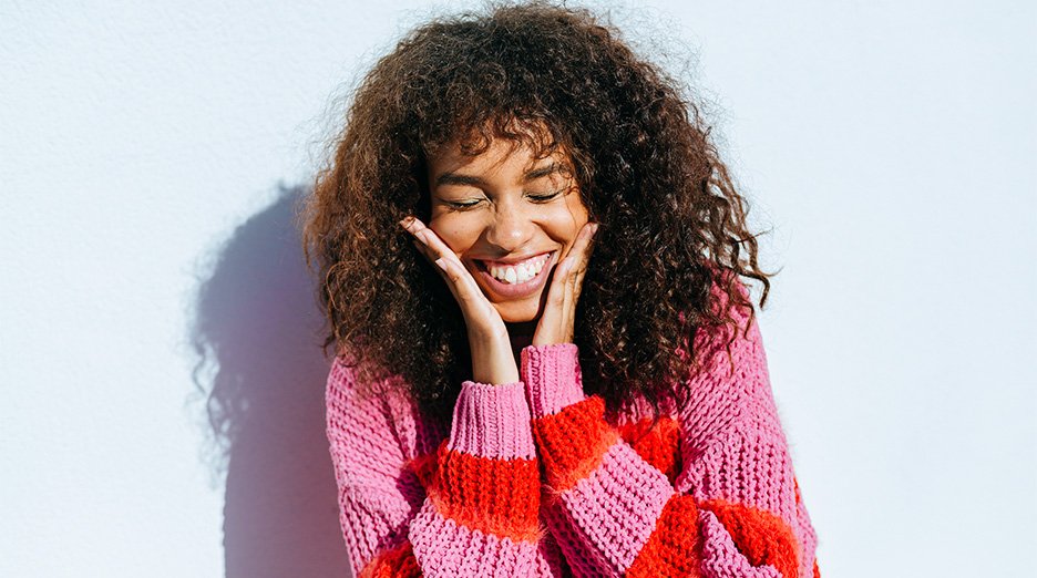 Woman with long and curly hair smiling with hands close to her face