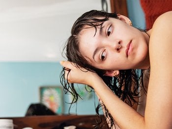 A person holding their head, using a smoothing shea butter cream for frizzy hair.
