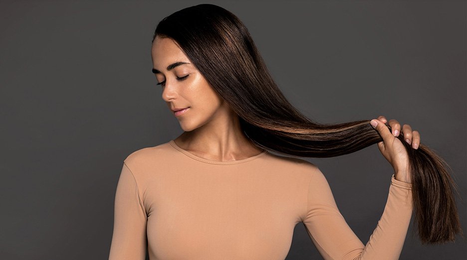 Brunette girl with long straight and shiny hair beauty skin woman holding her strong and healthy hair in her hands over grey background cosmetic hair beauty salon concept