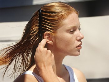 A close-up of a red-haired woman carefully brushing a section of her hair.