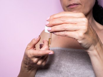 Hands hold a bottle of hair oil, preparing for a deep conditioning treatment to help with detangling.