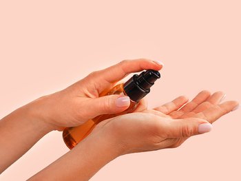 A person holds a small bottle of hair treatment, possibly a serum or leave-in conditioner, in their hands, ready to apply.