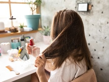 Woman spraying clear substance to brown hair in preparation for heat styling.