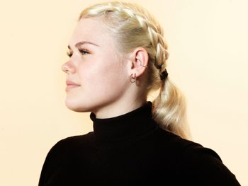 Young blonde woman in black turtleneck, looking away from camera to show off Dutch-braid style.