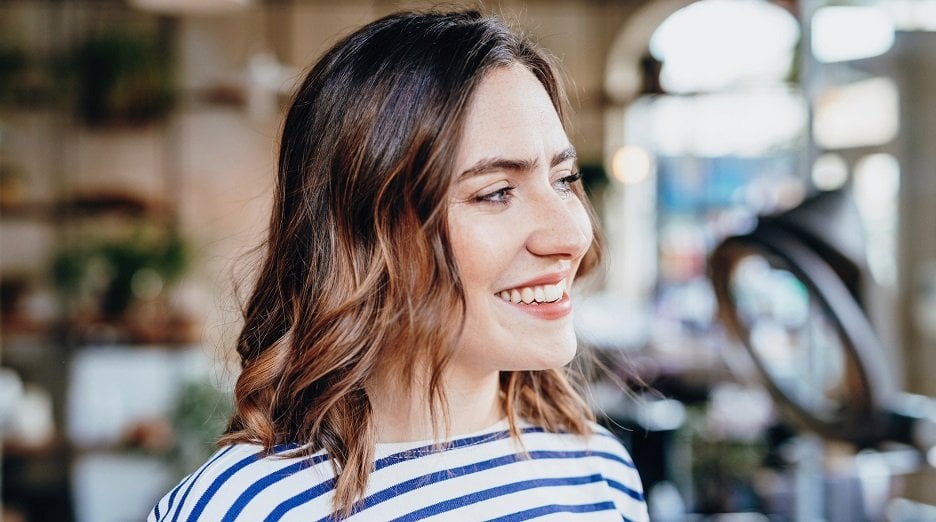 Brunette woman with light brown balayage smiling while looking to the side.