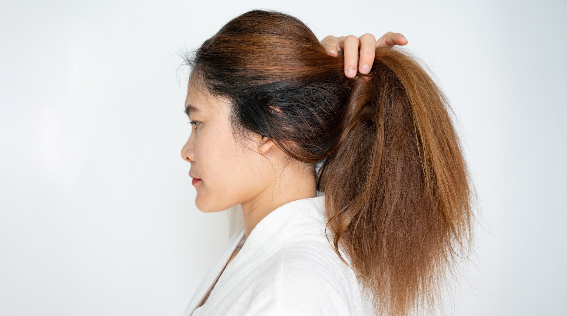 A person pulling their dry, frizzy hair into a ponytail.