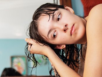 Woman leaning over as she scrunches her shoulder-length 2B wavy hair. Hair is still damp/wet from washing.