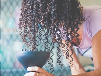 Woman bending forward with 3C curly hair flipped over her face. She is gently diffusing her curls upward.