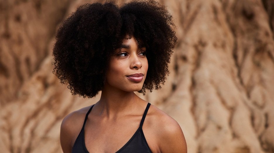 Fit woman with 4B curly hair standing outdoors after a late afternoon trail run.