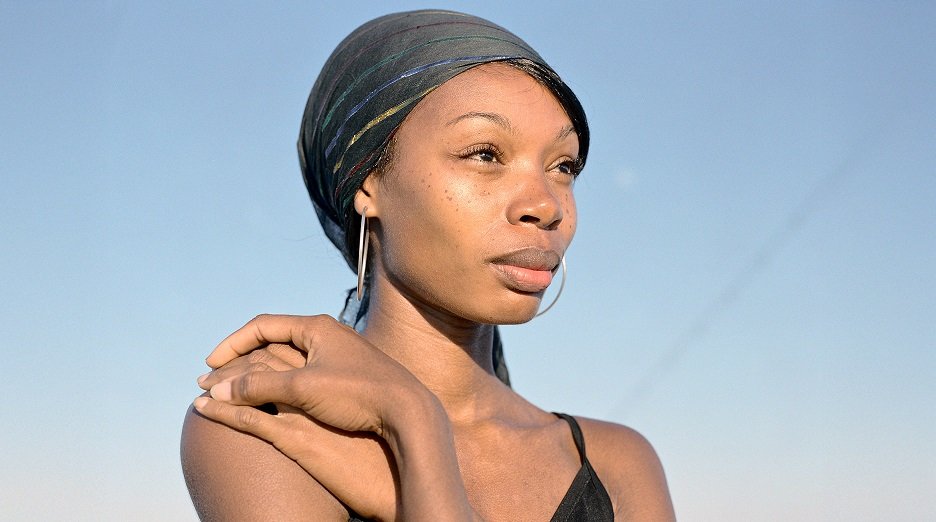 Woman wearing a headscarf and hoop earrings against a clear blue sky.
