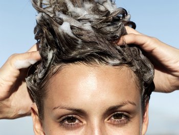 A woman with brown hair rinses her hair in the shower, clearly demonstrating the act of hair washing.