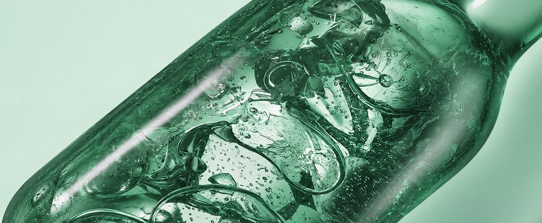 A macro close-up of a clear green gel keratin formula swirling with bubbles inside a translucent bottle, illuminated by a soft light beam.