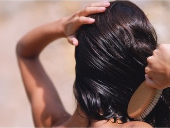 A woman with dark, glossy hair brushes her head, demonstrating the shine and health that biotin can contribute to.