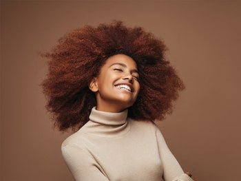 A woman with a large, voluminous curls smiles radiantly, showcasing the full, bouncy hair that biotin can help achieve.