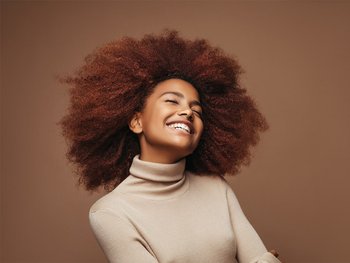 A woman with a large, voluminous curls smiles radiantly, showcasing the full, bouncy hair that biotin can help achieve.