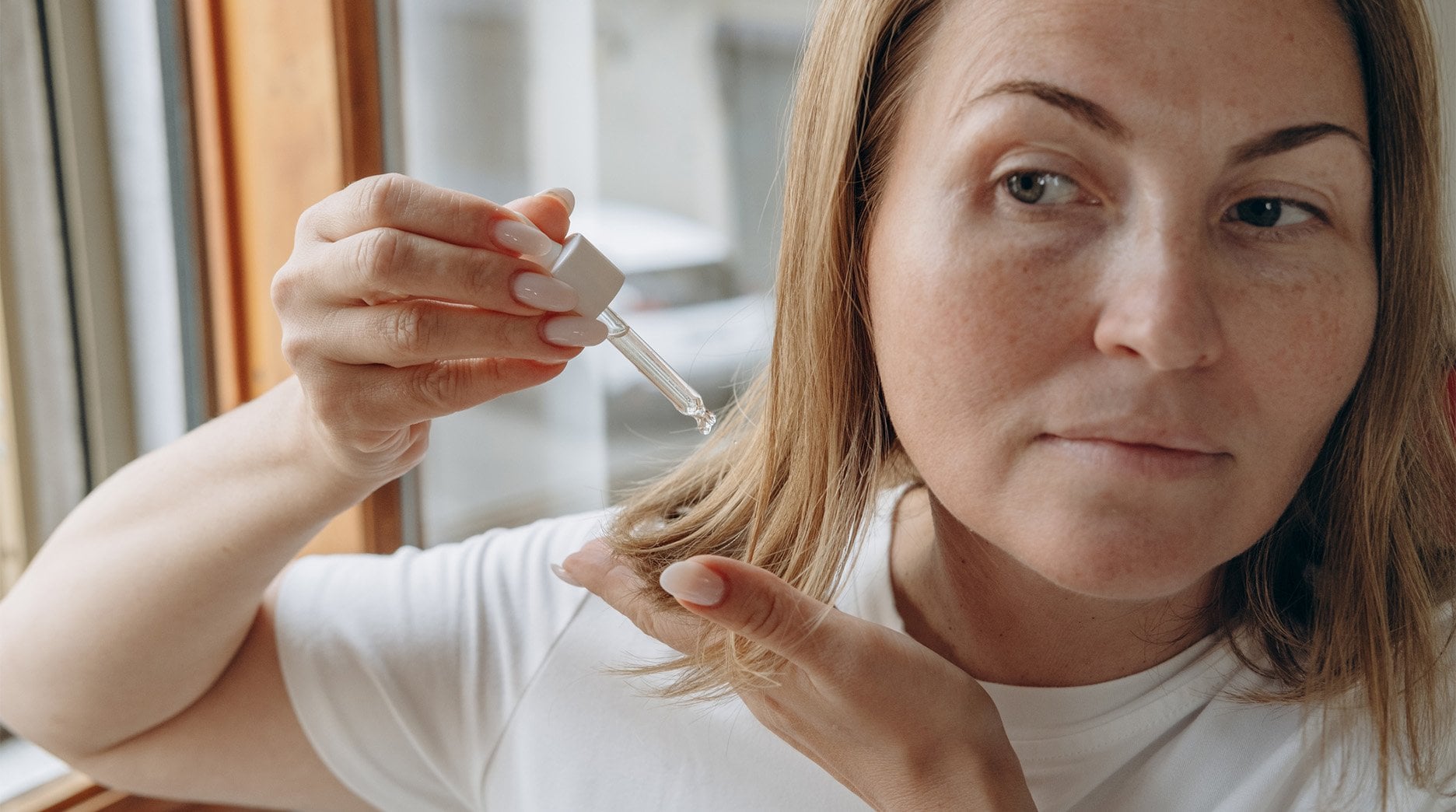 A person with straight hair applies argan oil using a dropper, demonstrating a common application method.