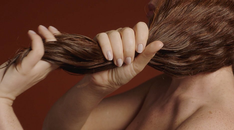 Hands hold a section of brown hair.