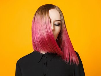 Model with long bob brown and pink hair looking down to the side in front of an orange background.
