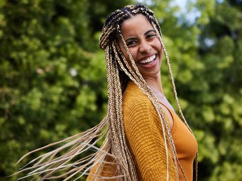 Laughing young woman twirling her long braided hair outside in summer