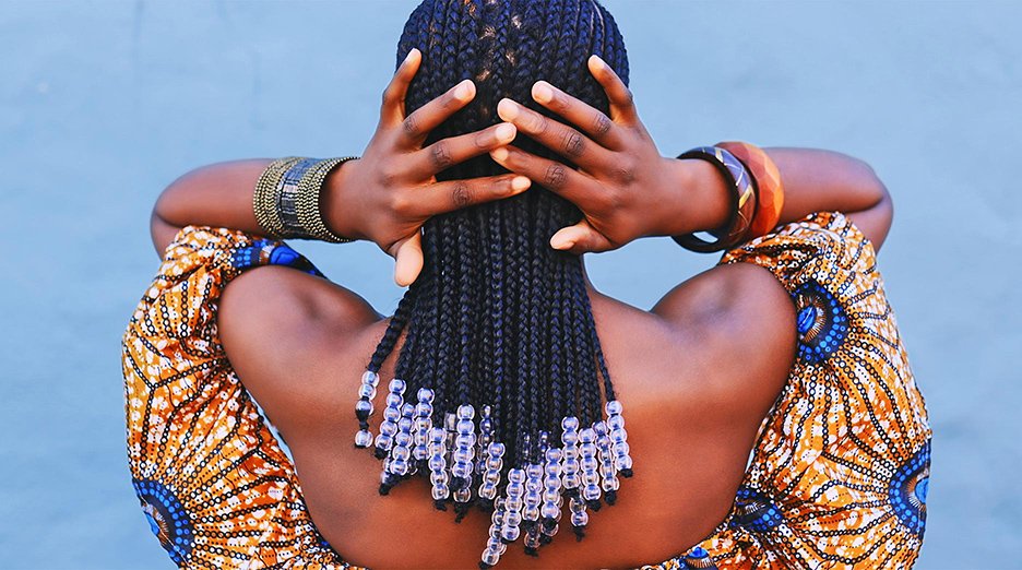 Rearview shot of a young woman wearing traditional African clothing and feeling her hair against a blue background