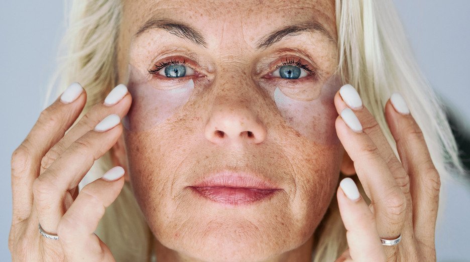 A close-up, straight-on image of a mature woman with pale blonde hair and blue eyes.