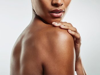 A close-up of a person's shoulder and back, showcasing smooth, healthy skin. Their hand is gently resting on their opposite shoulder.