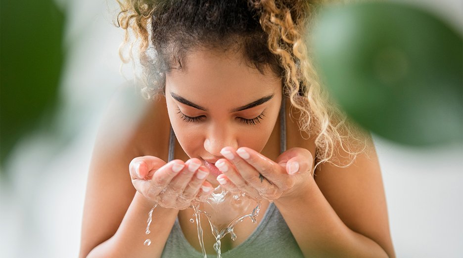Mixed race woman splashing water on face.
