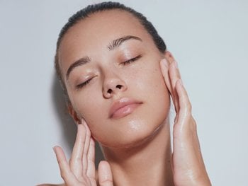 A person gently massages their face with their eyes closed, likely after applying moisturizer.