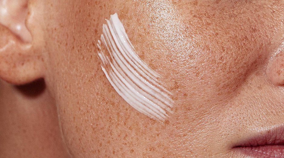 Streaks of white moisturizer are visible on a person's cheek, close to their ear.