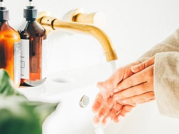 Hands are being washed under a running faucet, visualizing the cleansing step.