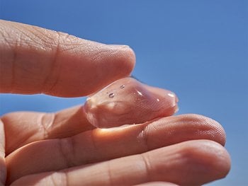 A clear, gel-like moisturizer is being held on fingertips.