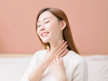 A woman gently massages her neck demonstrating the application of an exfoliating scrub.