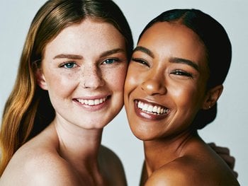 Two smiling women with different skin tones and clear complexions represent the positive results of an effective oily skincare routine.