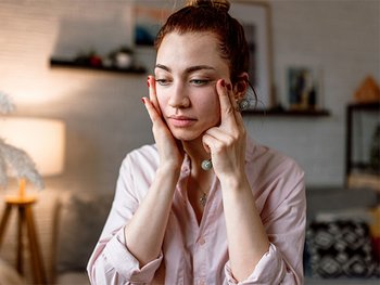 A woman with a concerned expression gently touching her face, suggesting skin discomfort, sensitivity, or the need for a soothing skincare solution.