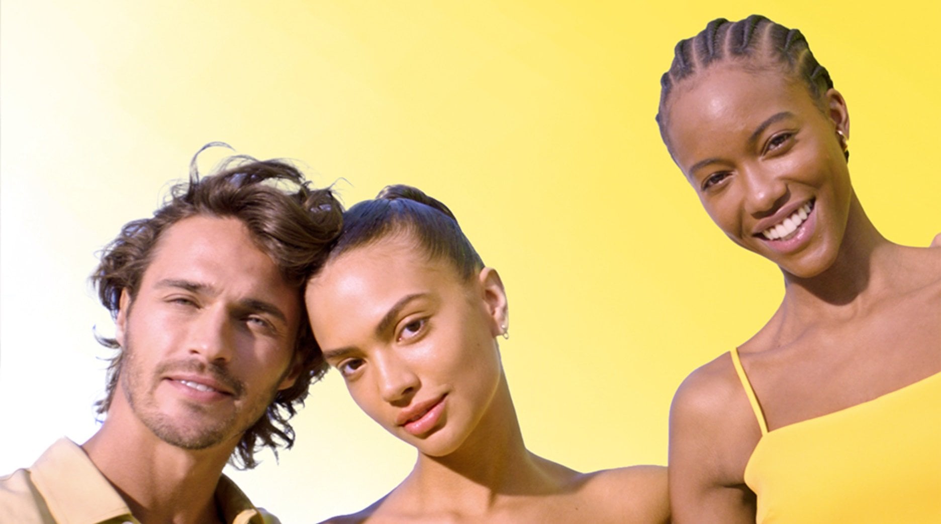 Shot of diverse models smiling at camera. One male and two females, all with clear glowing skin.